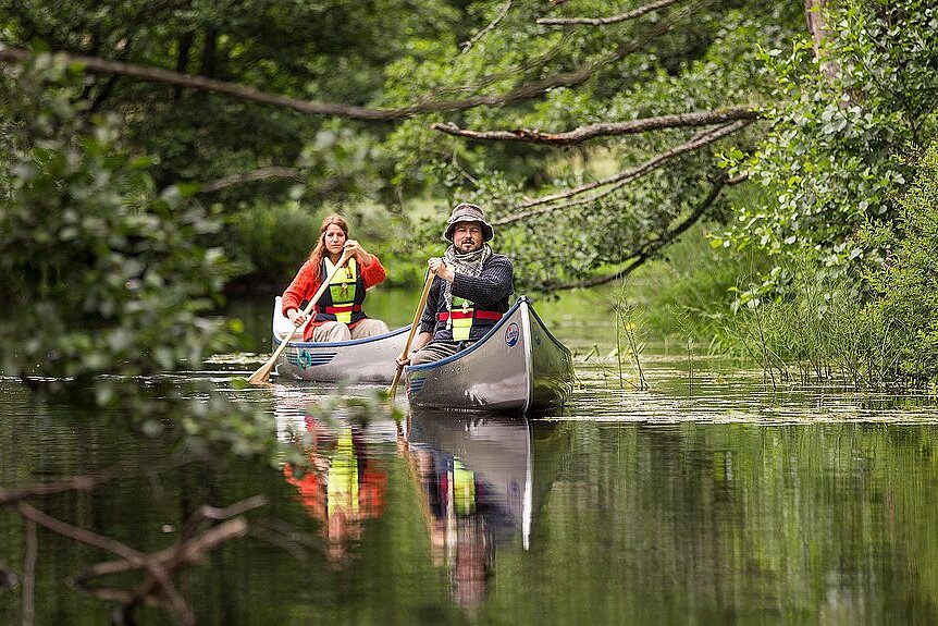 Dieses Bild zeigt zwei Kanus auf einem Fluss in einer Naturlandschaft.