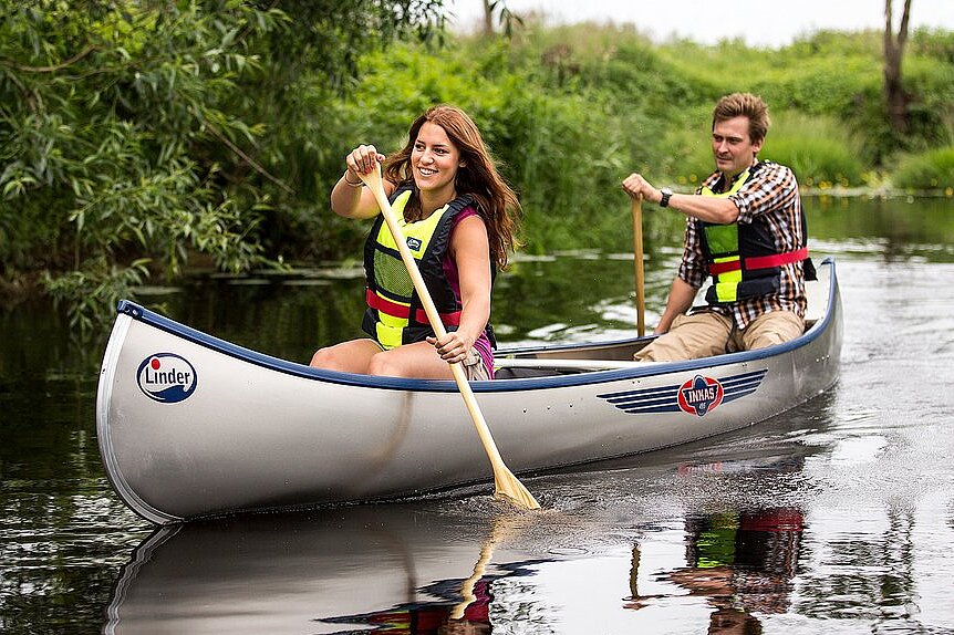 Dieses Bild zeigt eine Frau und einen Mann paddelns in einem Kanu von einer Naturflusslandschaft umgeben.