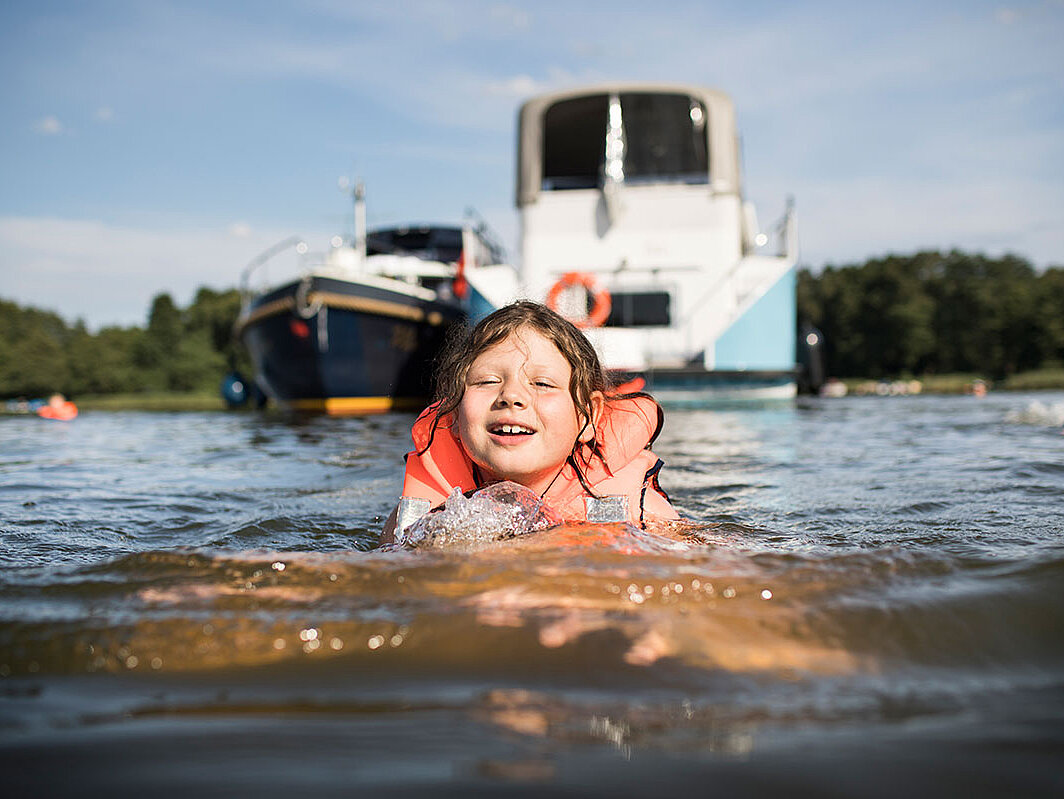 Das Bild zeigt ein Kind schwimmend vor einer Charteryacht.