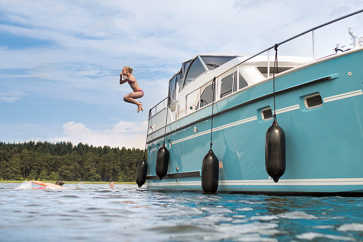 Ein Kind spring von einer Yacht in einen See.